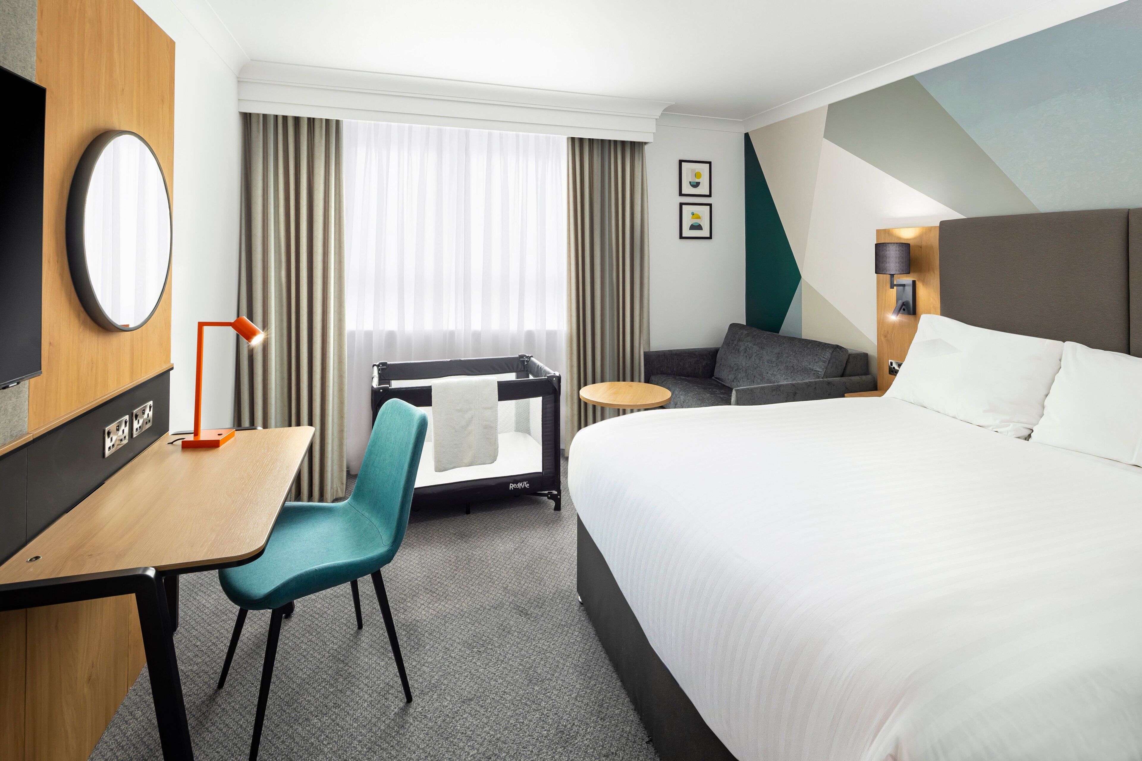 A hotel room with a large bed, a desk with a chair, a TV, and a window with curtains.