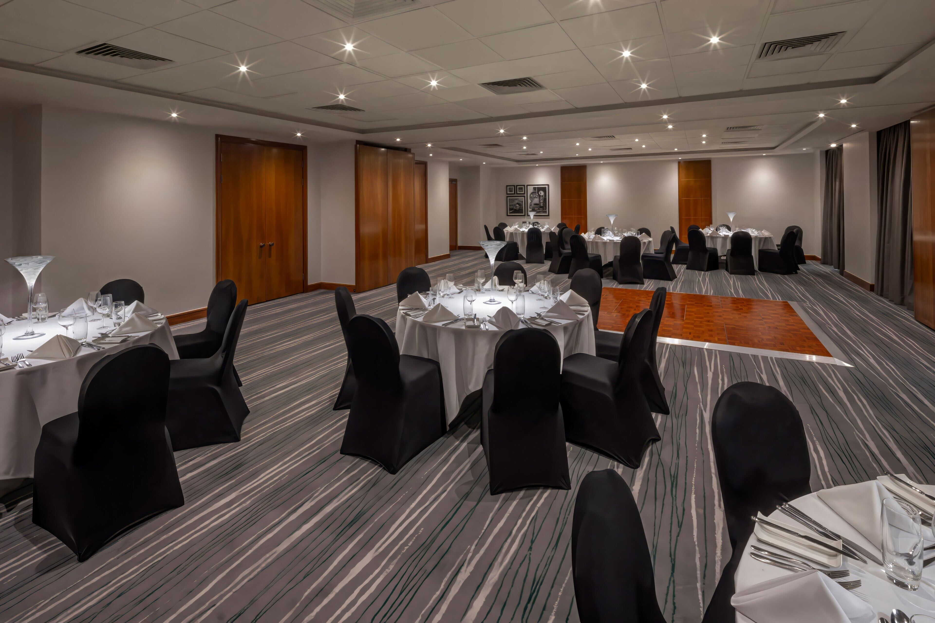 A conference room with round tables, black chairs, and white tablecloths.
