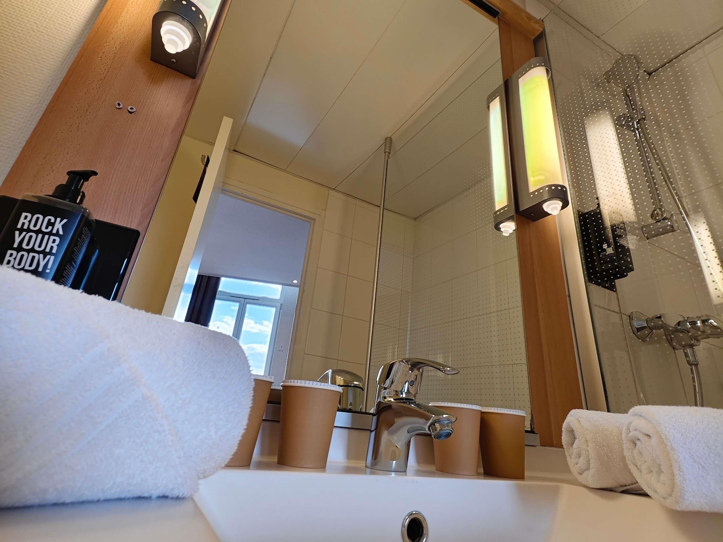 A bathroom with a sink, mirror, towel, shower, and a bottle labeled 'ROCK YOUR BODY!'