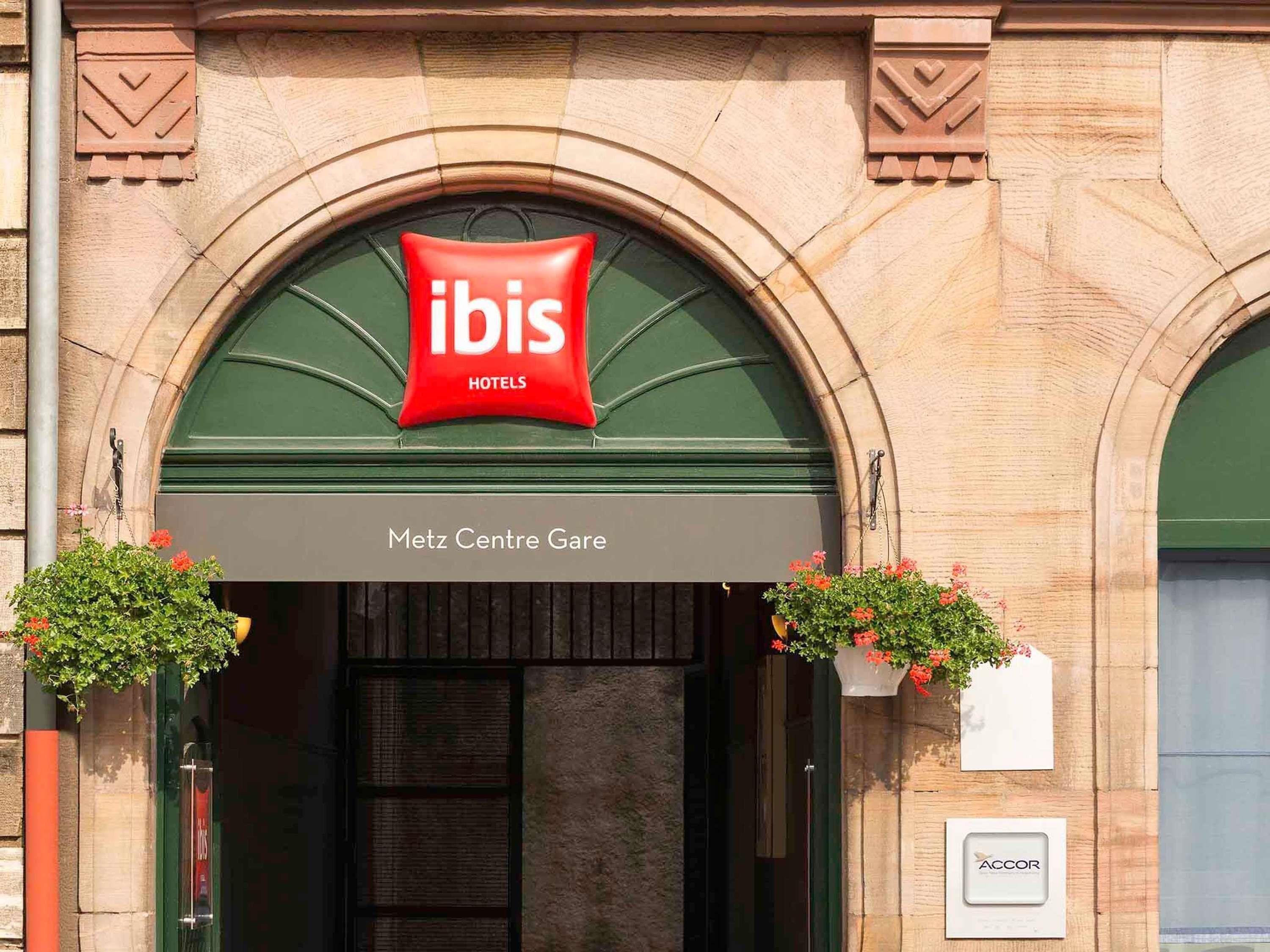 Entrada de un hotel con un arco, un letrero rojo de 'ibis Hotels' y un letrero que dice 'Metz Centre Gare'.