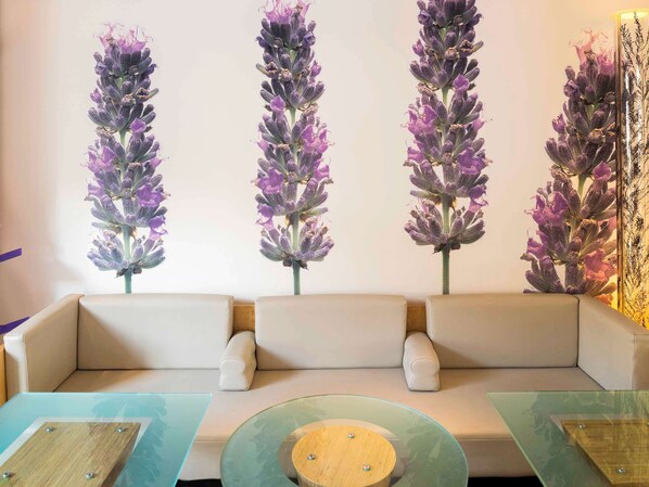A modern living room with a beige sofa, glass coffee tables, and wall-mounted floral decorations. - ibis Metz Centre Gare (Metz)