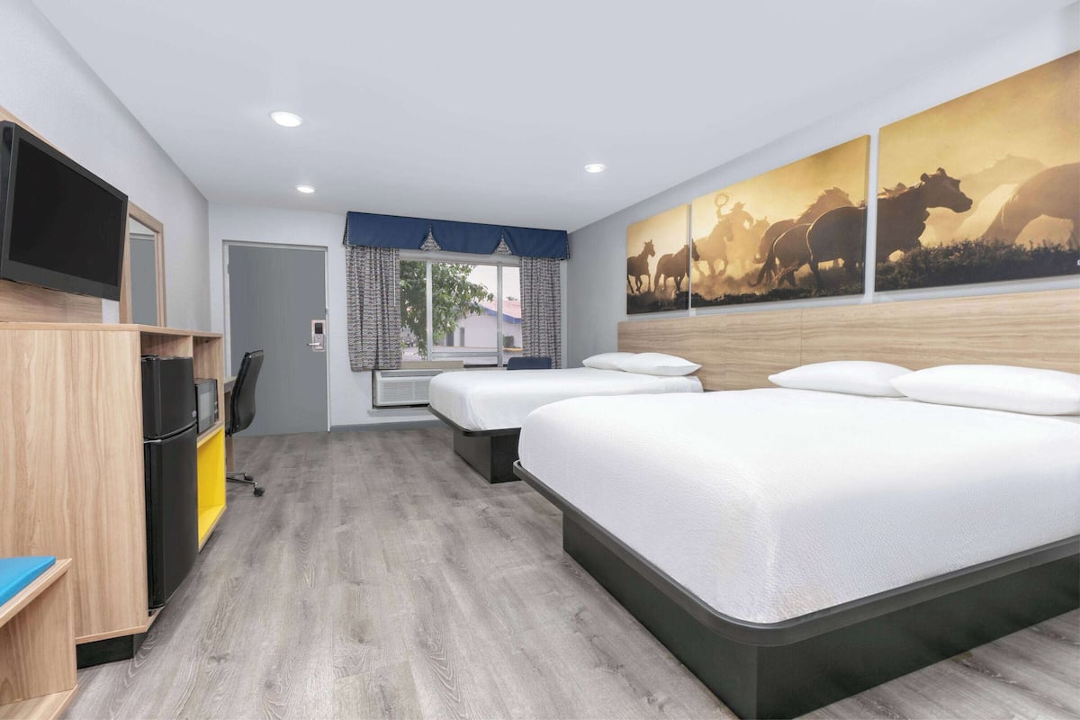 A hotel room with two beds, a TV, a desk, and a window with curtains.