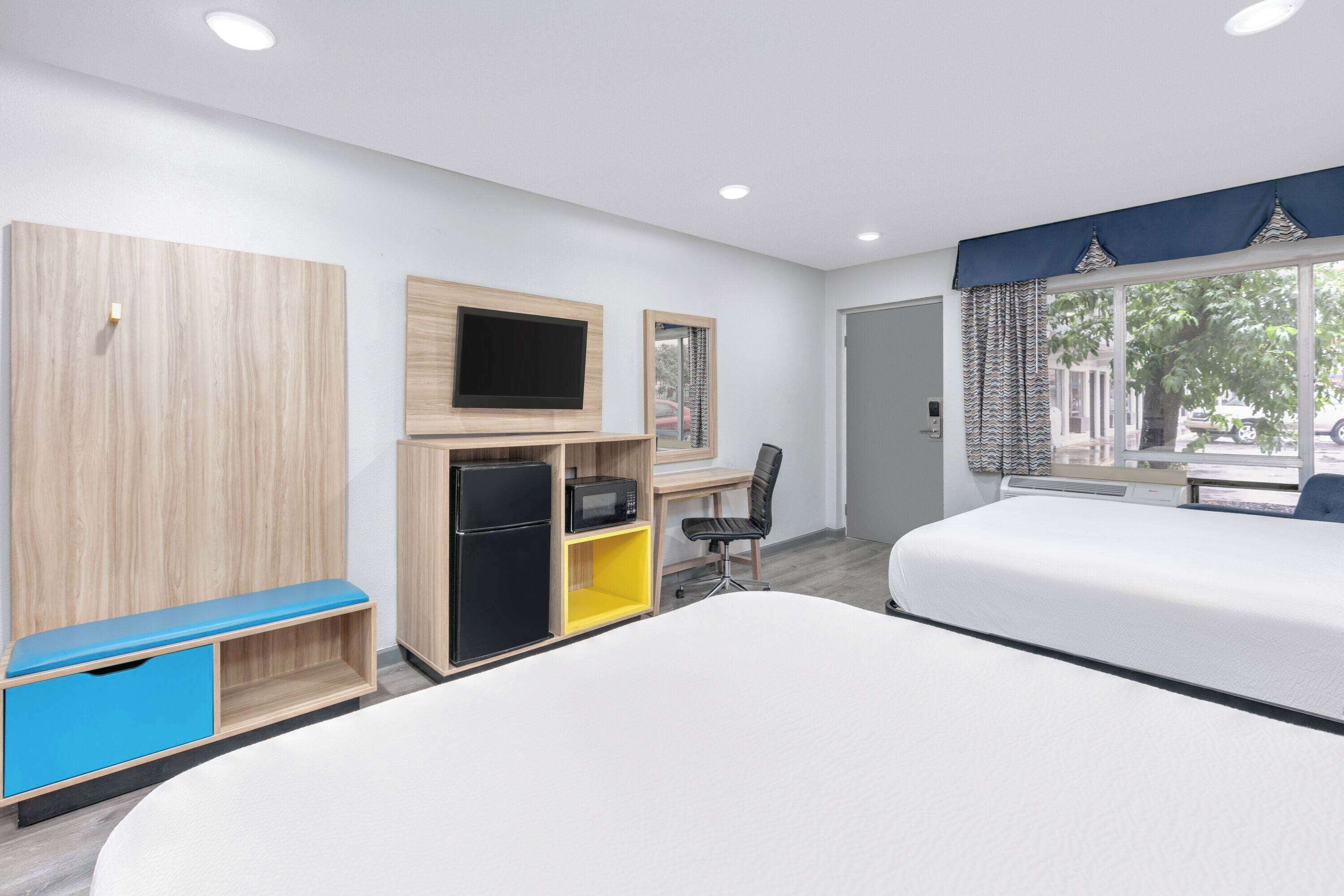 A hotel room with two beds, a desk with a chair, a TV, a wardrobe, and a window with curtains.