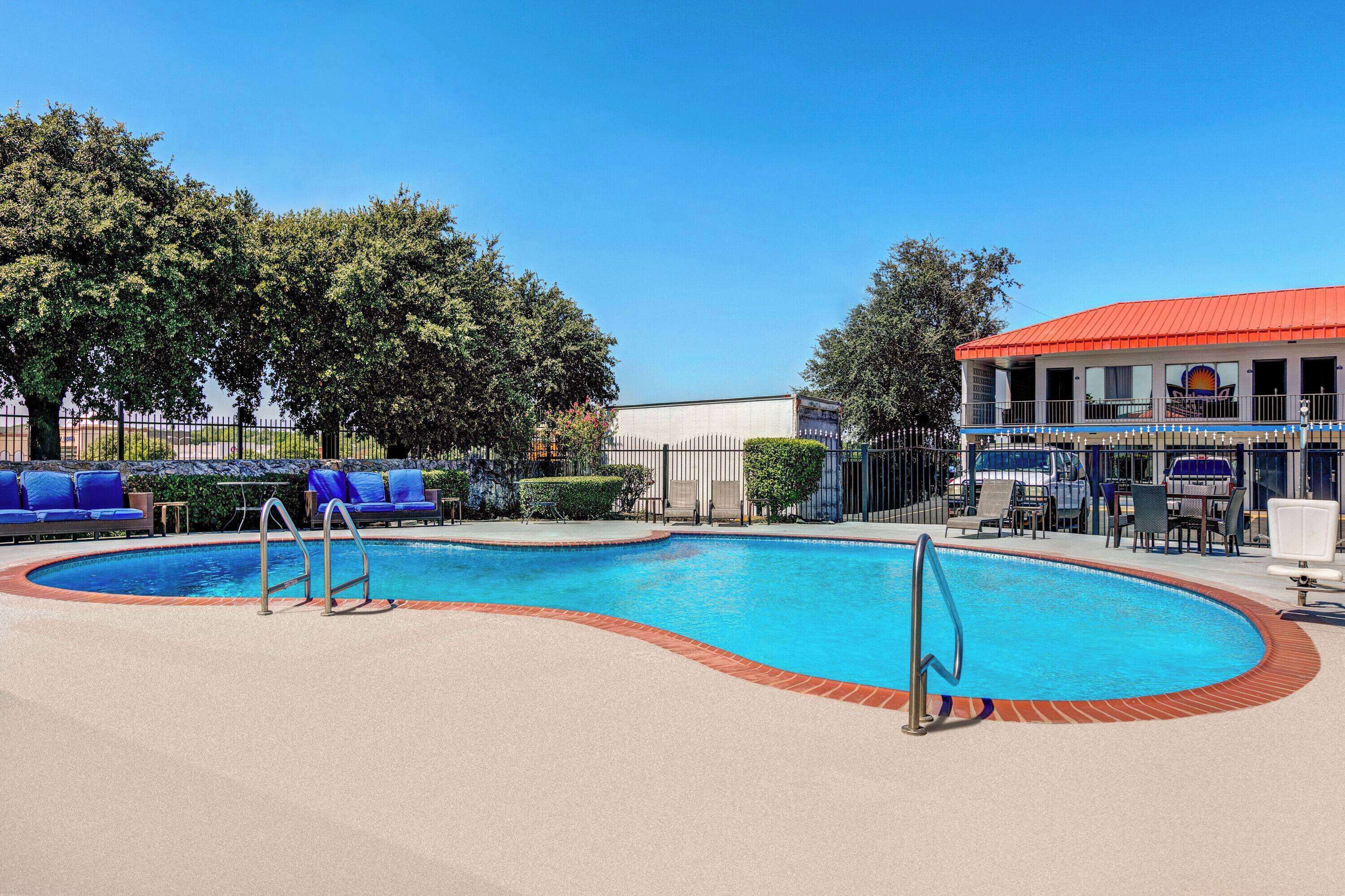 Ein Swimmingpool mit blauen Liegestühlen, einem eingezäunten Bereich und einem Gebäude mit rotem Dach.