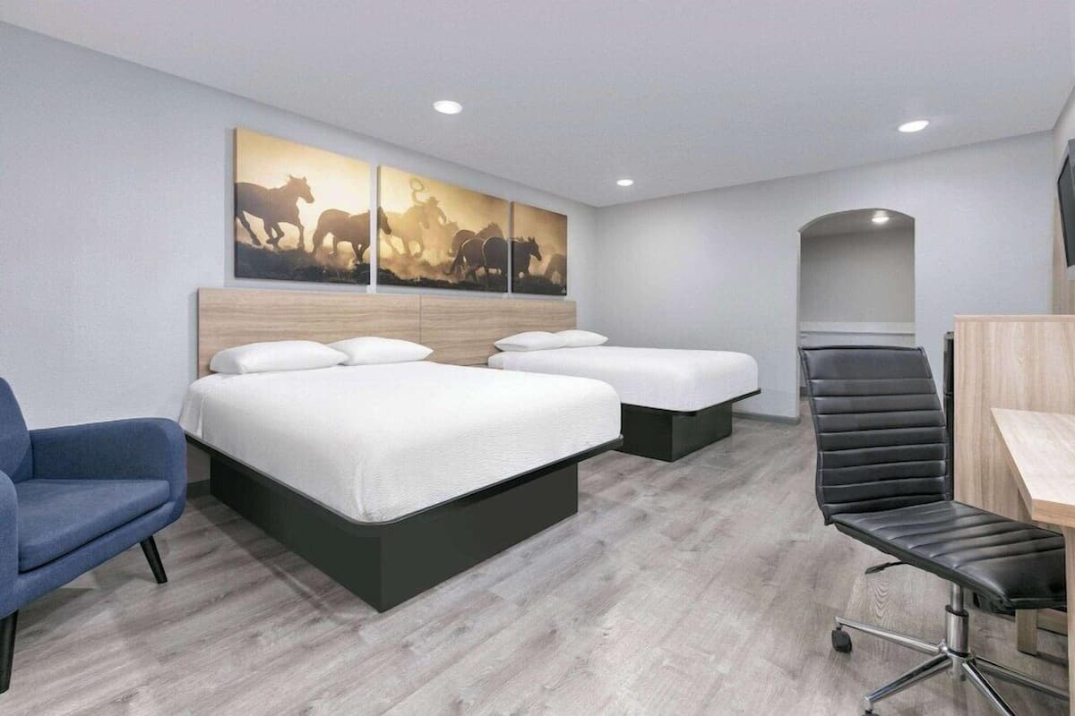 A hotel room with two beds, a desk, a chair, and a wall-mounted artwork.