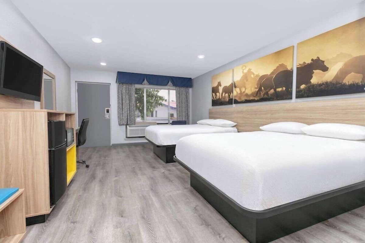 A hotel room with a large bed, a TV, a desk, and a window with curtains.