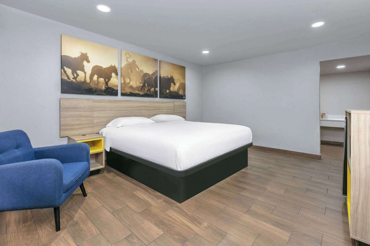 A modern hotel room with a large bed, a blue armchair, and wooden flooring.