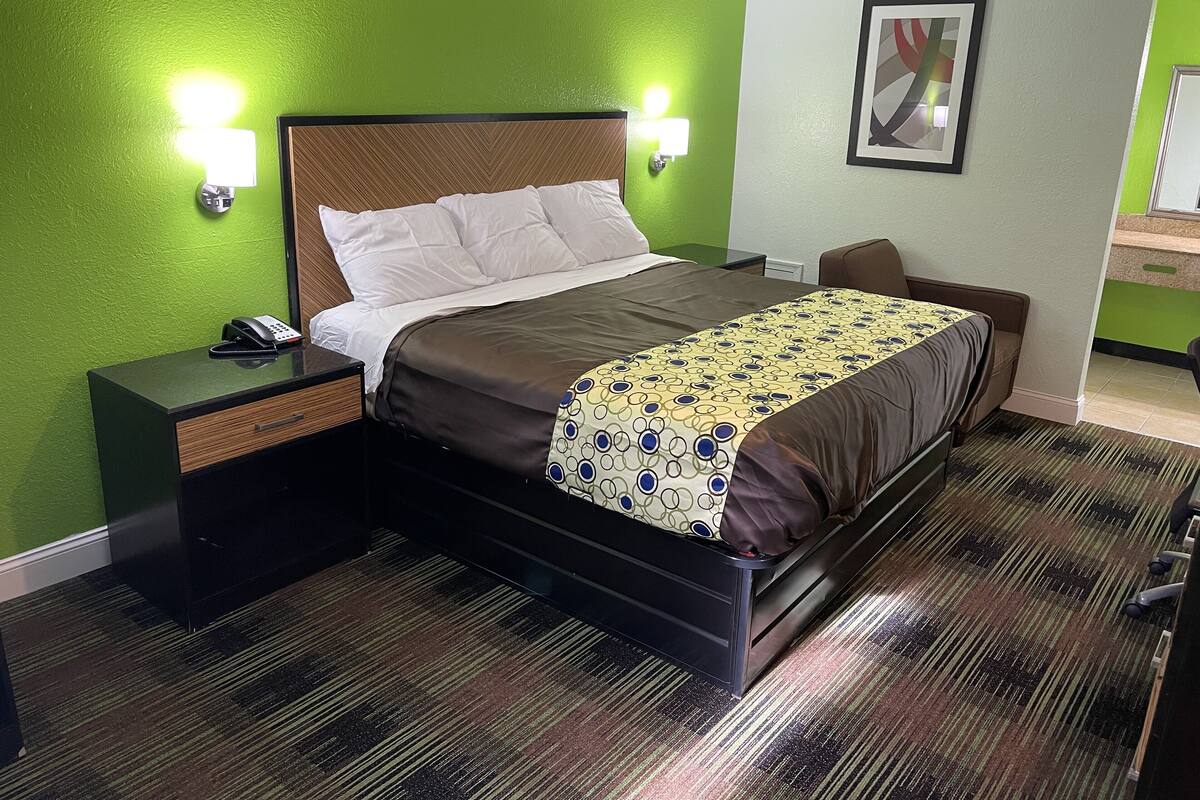 Una habitación de hotel con cama, mesitas de noche, teléfono y lámpara de pared.