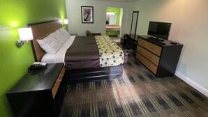 Habitación de hotel con cama, mesita de noche, cómoda, televisor y baño visible a través de una puerta abierta.