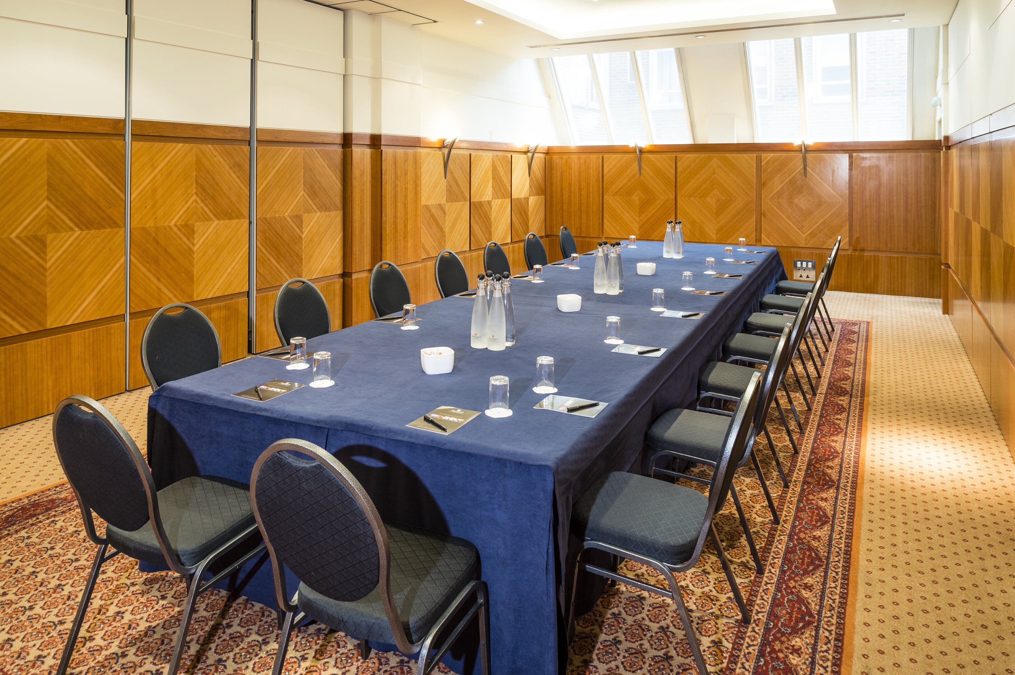Un salón de conferencias con una larga mesa, sillas y suelo alfombrado.