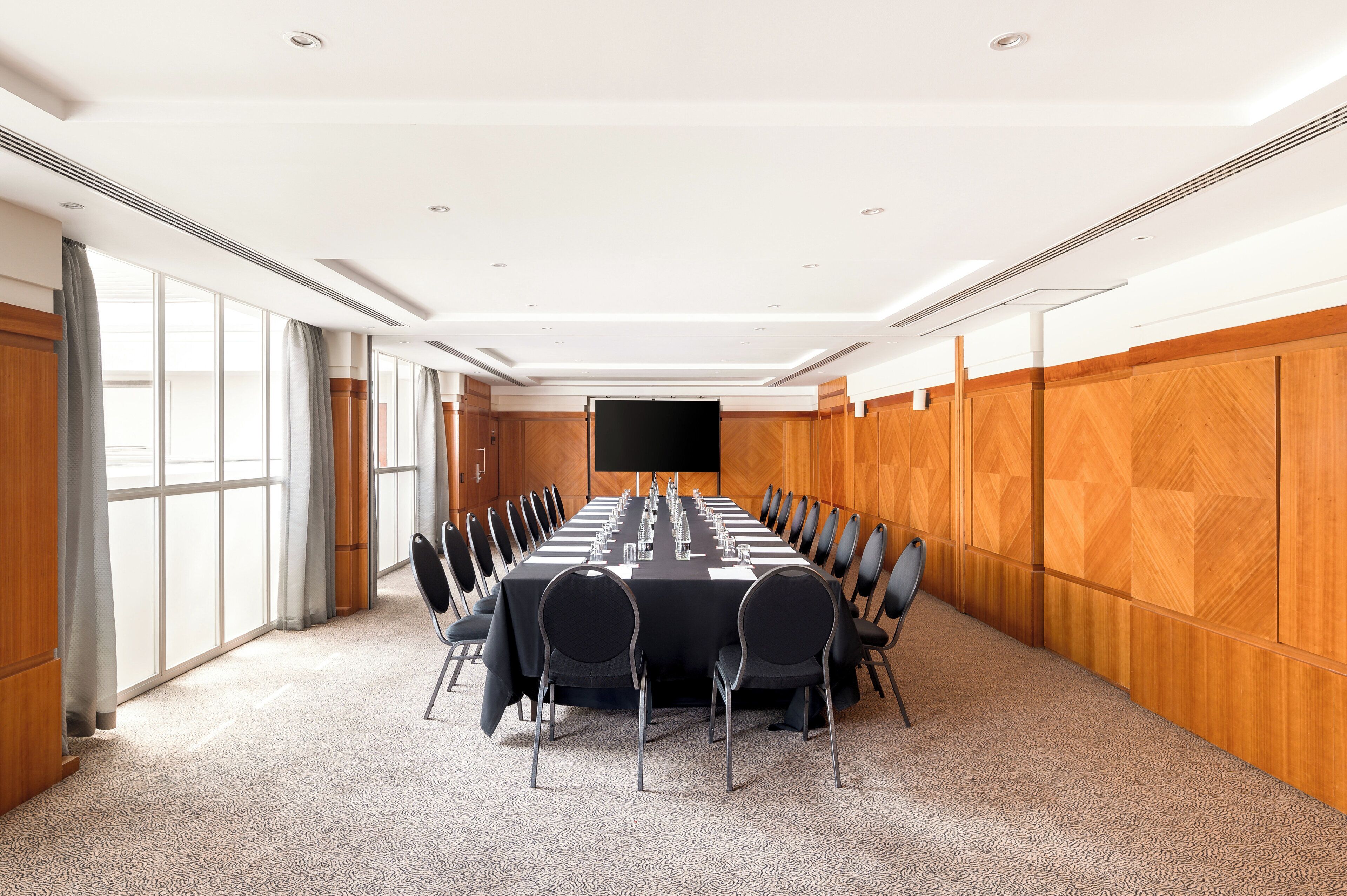 A conference room with a long table, chairs, and a large screen.