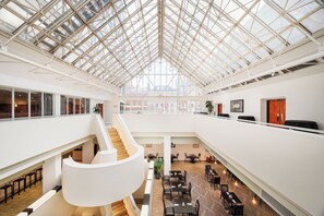 Een ruime atrium met een hoge plafond, een spiraaltrap in het midden en meerdere zithoeken.