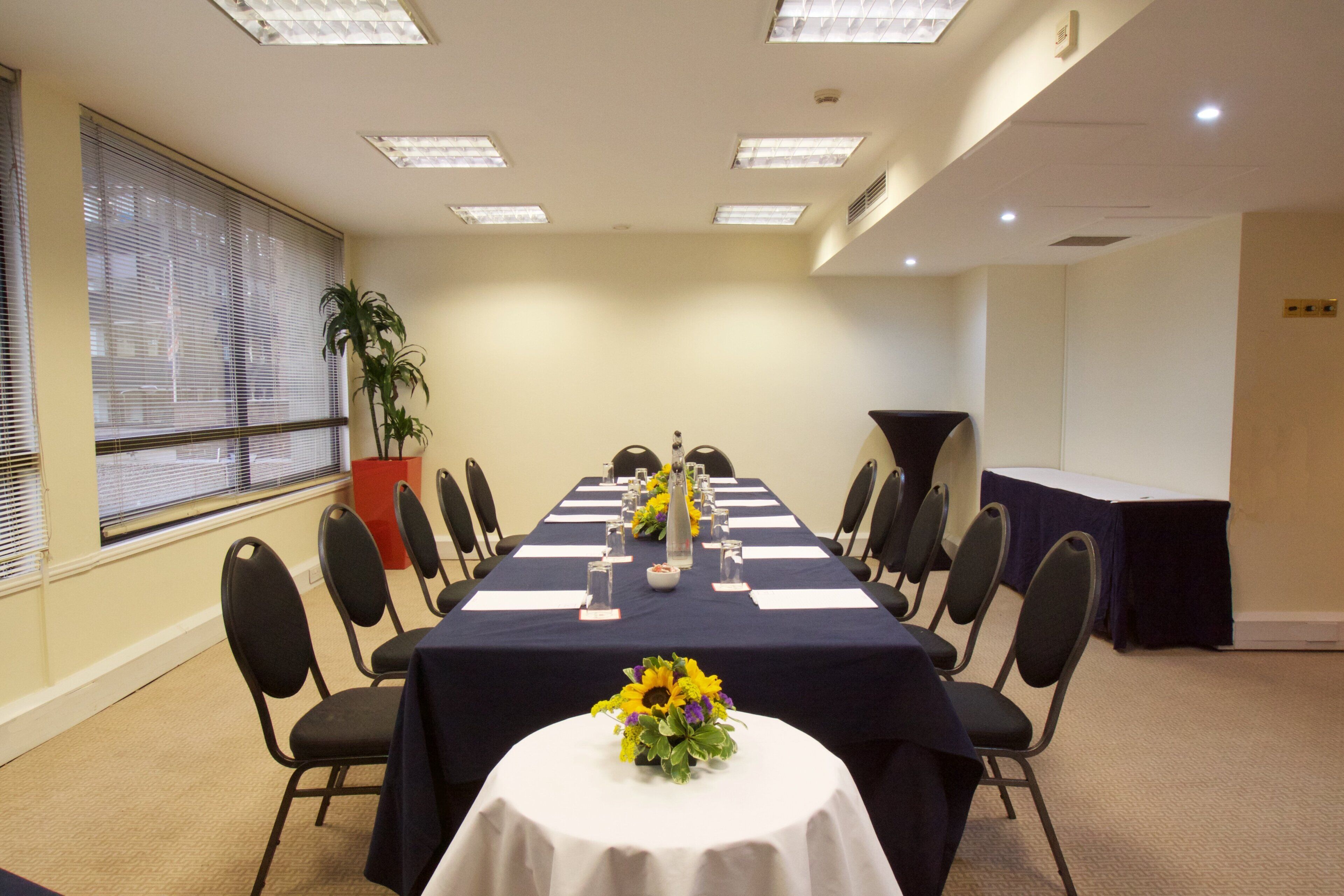 A conference room with a long table, chairs, a potted plant, and a podium.