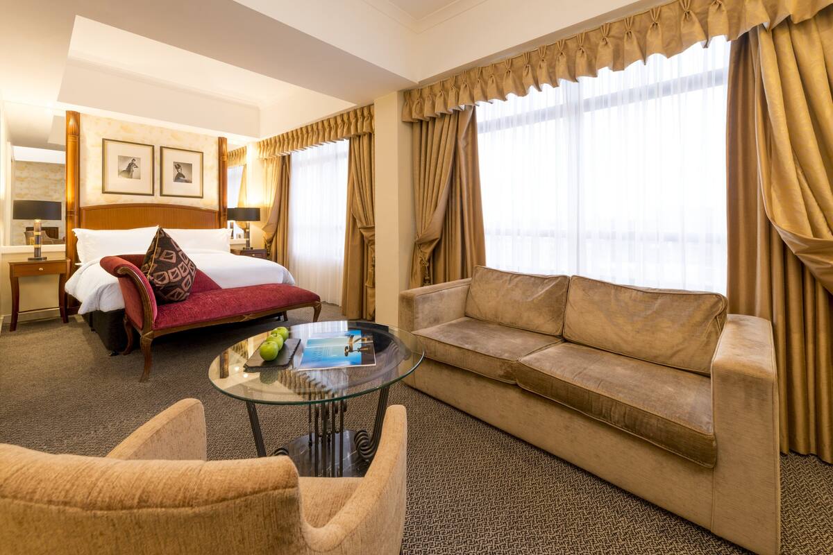 A hotel room with a bed, a sofa, a glass coffee table, and a chair.