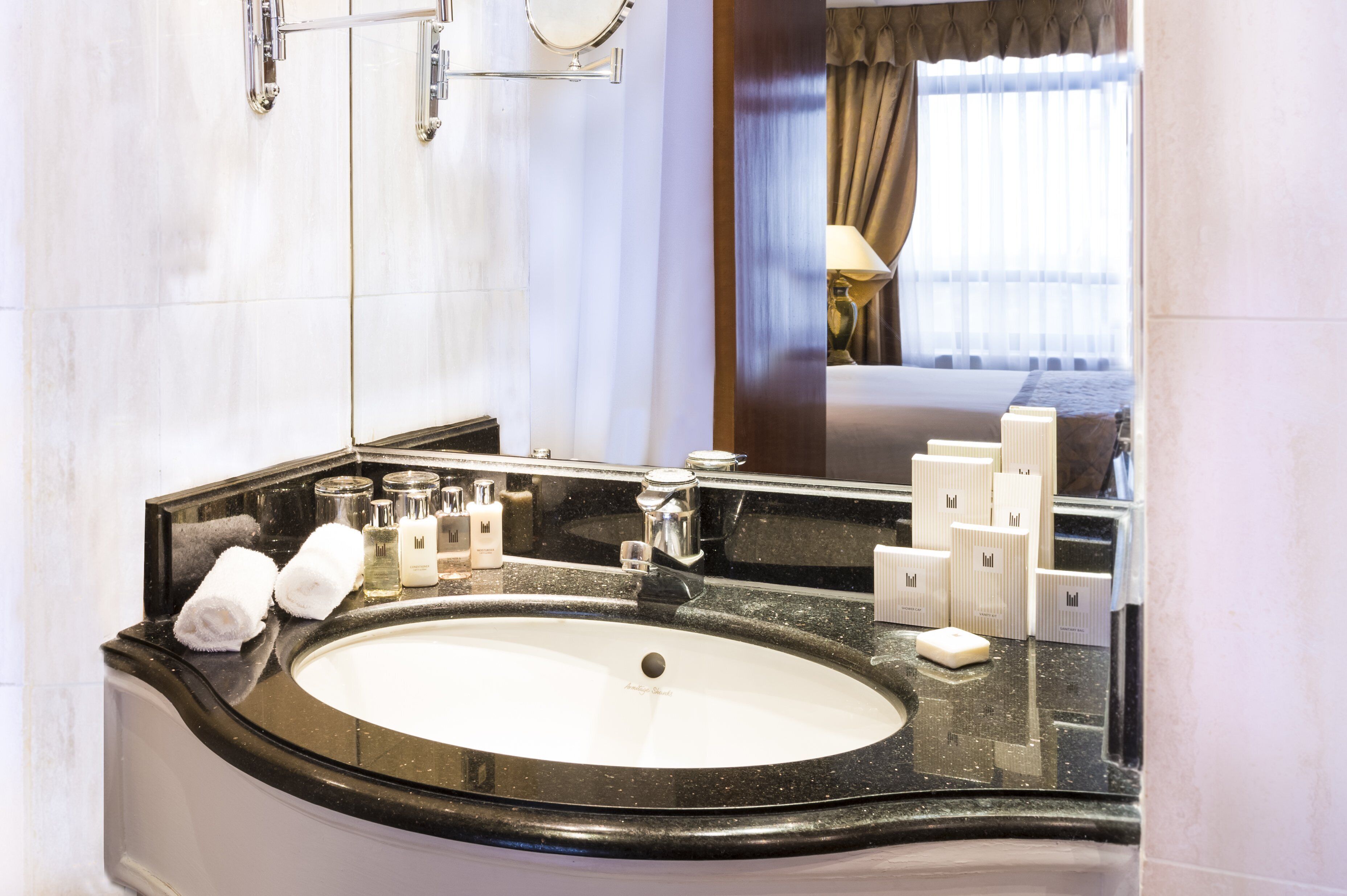 A hotel bathroom with a large sink, a mirror, and toiletries.