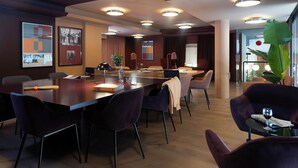 A modern conference room with a long table, purple chairs, and ceiling lights.