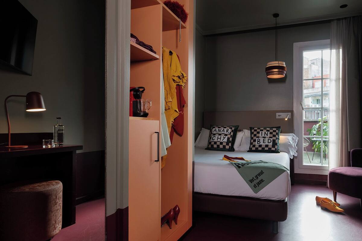 A bedroom with a bed, a desk with a lamp, a chair, and a window with a view.