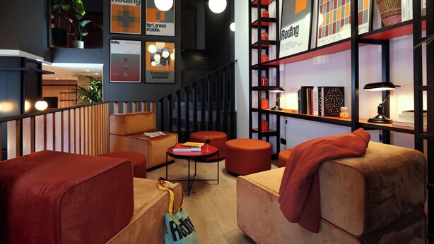 A modern interior with a staircase, red and beige seating, and a bookshelf with 'Reding' labels.