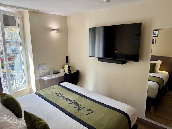 Habitación de hotel con una cama, televisión montada en la pared, mesita de noche con lámpara y ventana con vistas al exterior.