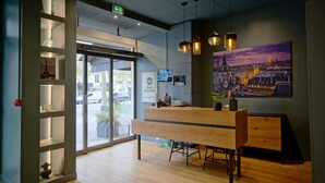 A reception area with a wooden desk, pendant lights, and a cityscape painting. - Best Western Hotel Le Montparnasse (Paris)