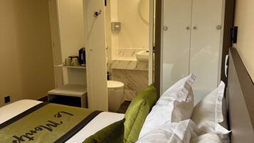 Una habitación de hotel con cama, armario, baño y una mesita con tetera.