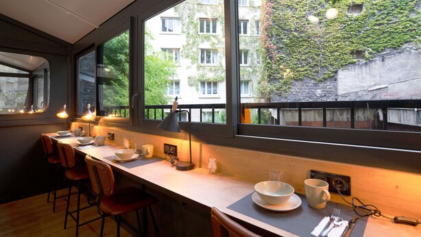 A modern kitchen with a long counter, bar stools, and a view of a building with ivy-covered walls. - Best Western Hotel Le Montparnasse (Paris)