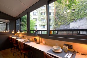 Una cocina moderna con una encimera larga, taburetes de bar y vista a un edificio con muros cubiertos de hiedra.