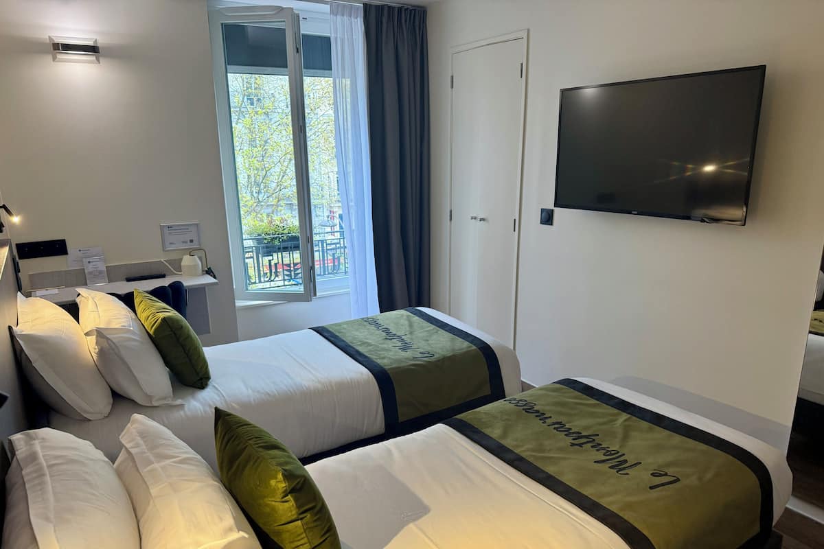 A hotel room with two beds, a TV, a window with curtains, and a desk with a lamp.