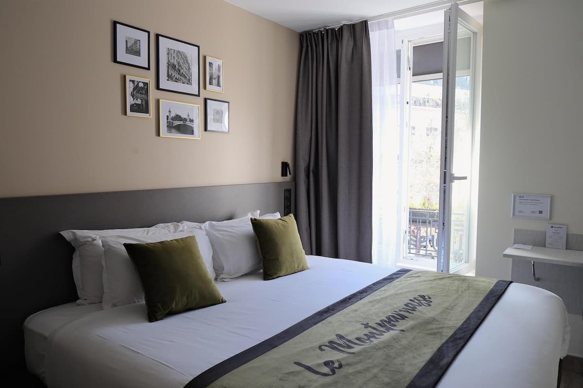 A hotel room with a bed, a window with curtains, and framed pictures on the wall.