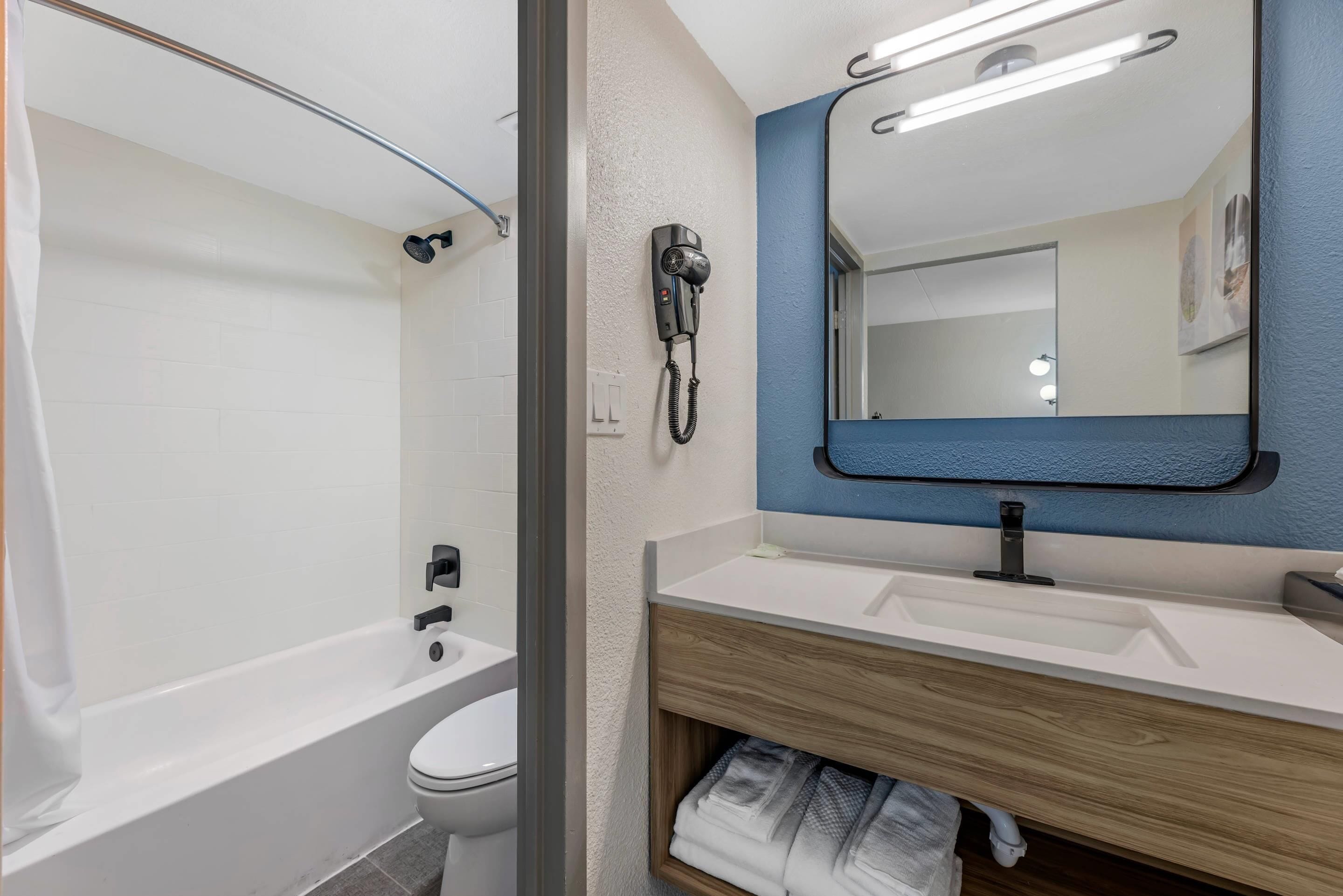 Uma casa de banho moderna com banheira, sanita, toucador com espelho e um secador de cabelo fixado na parede.