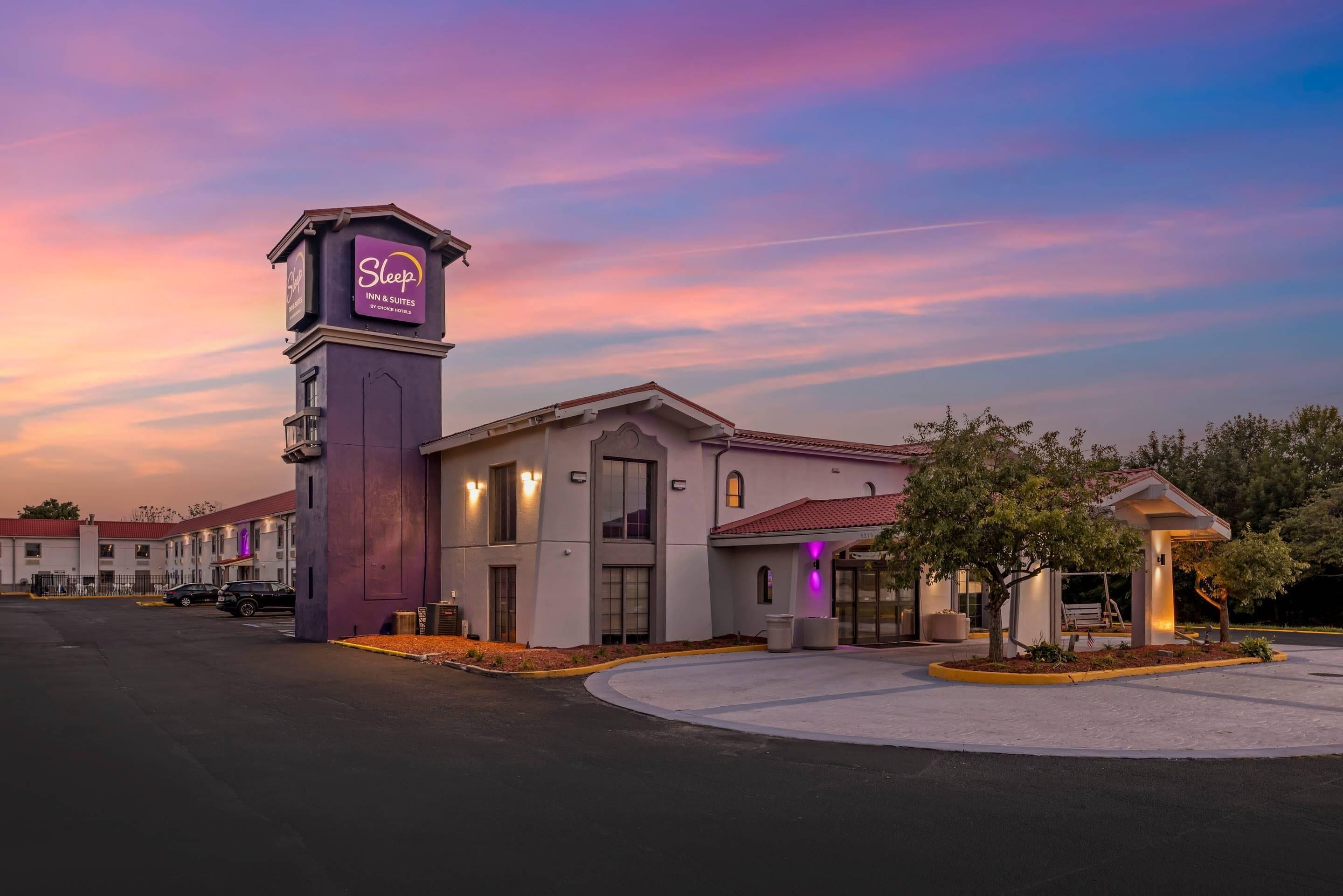 A Sleep Inn & Suites building with a clock tower, a covered entrance, and a parking lot.