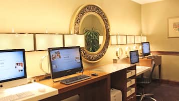 A hotel room with a desk, two monitors, a keyboard, a mouse, a printer, and a mirror.