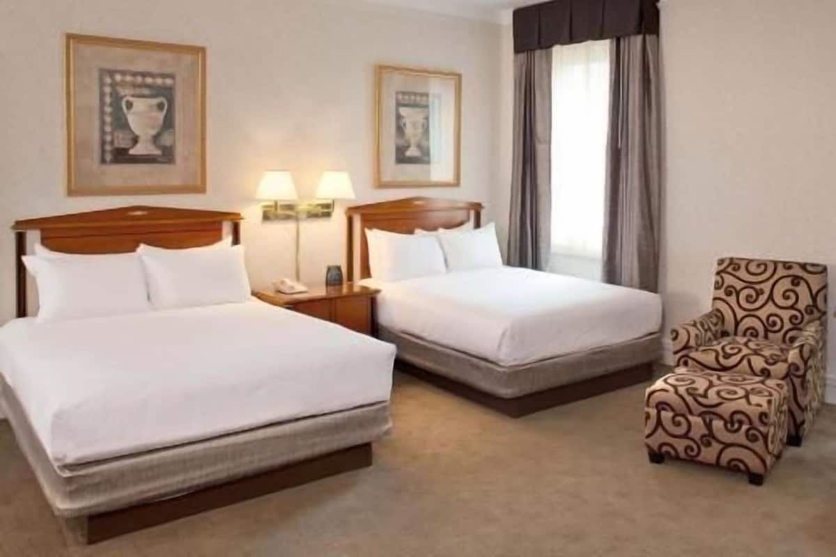 A hotel room with two beds, a chair, and framed artwork on the walls.