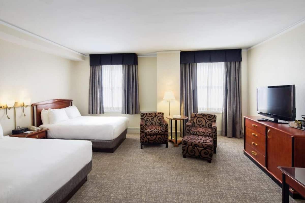 A hotel room with two beds, a TV, a desk, and a chair.