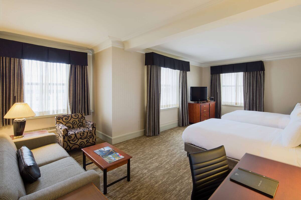 A hotel room with a bed, a sofa, a chair, a desk, a lamp, and a television.