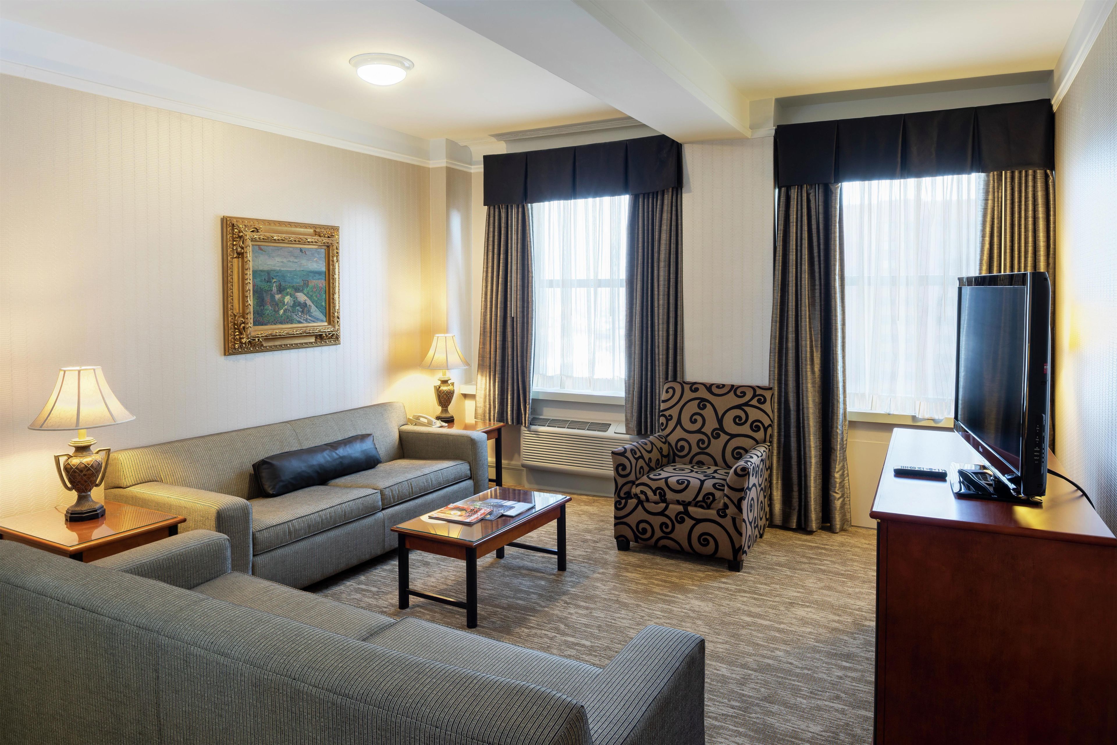 Une chambre d’hôtel avec un canapé, un fauteuil, une table basse, une télévision et un tableau au mur.