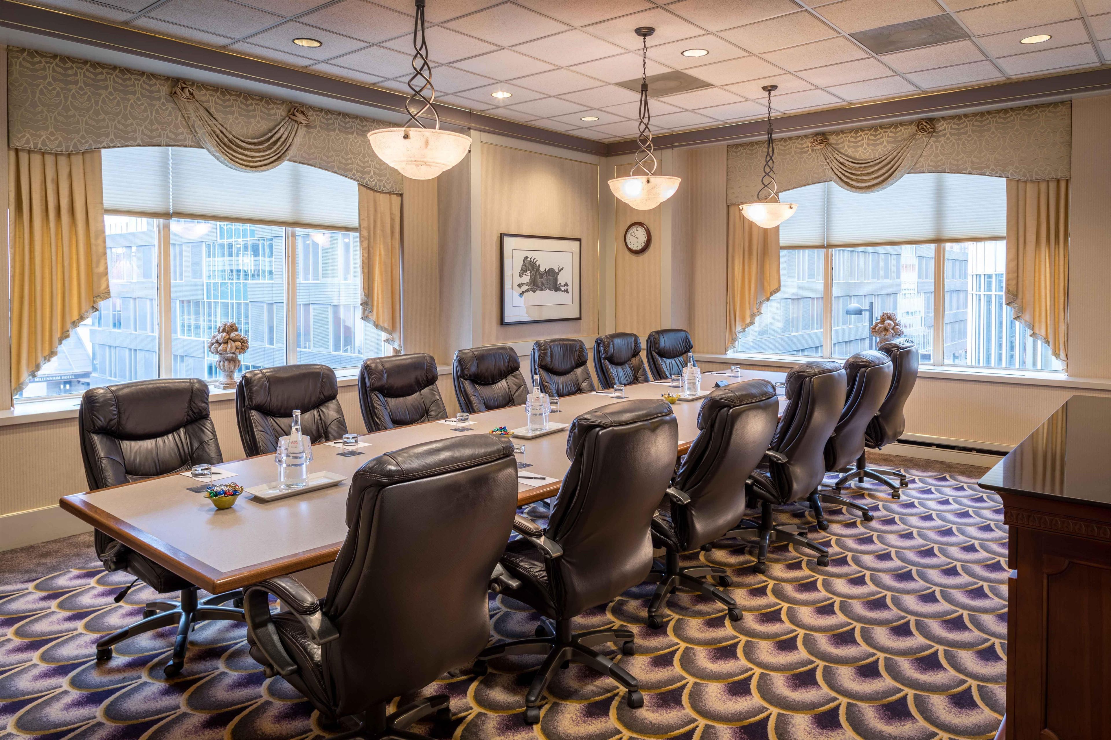 Une salle de conférence avec une longue table, des fauteuils en cuir et de grandes fenêtres.