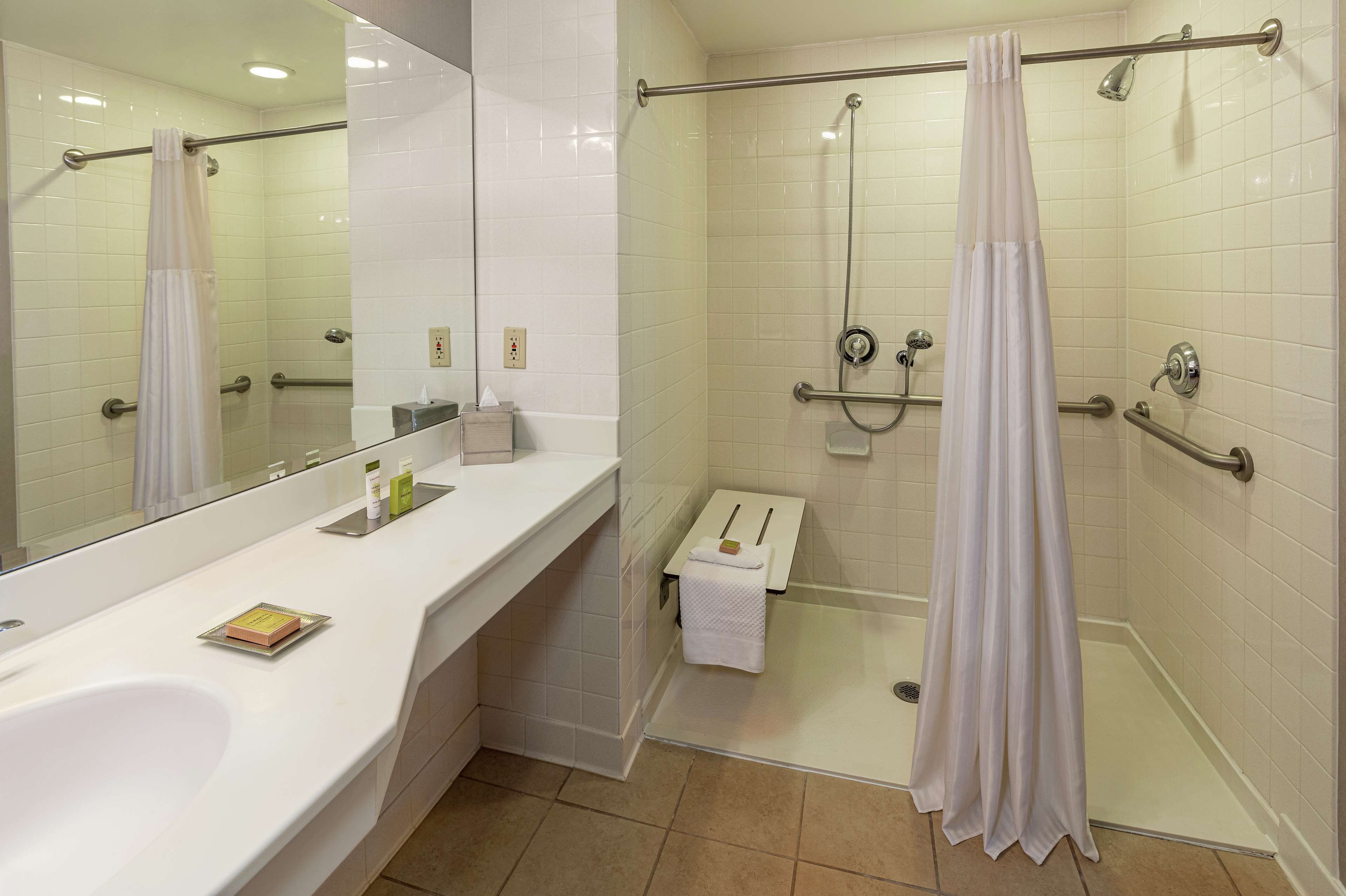 A modern bathroom with a large mirror, white sink, and a walk-in shower with a glass door.