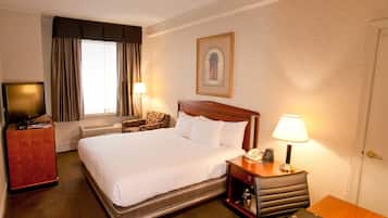 A hotel room with a large bed, a television, a desk with a lamp, and a chair.
