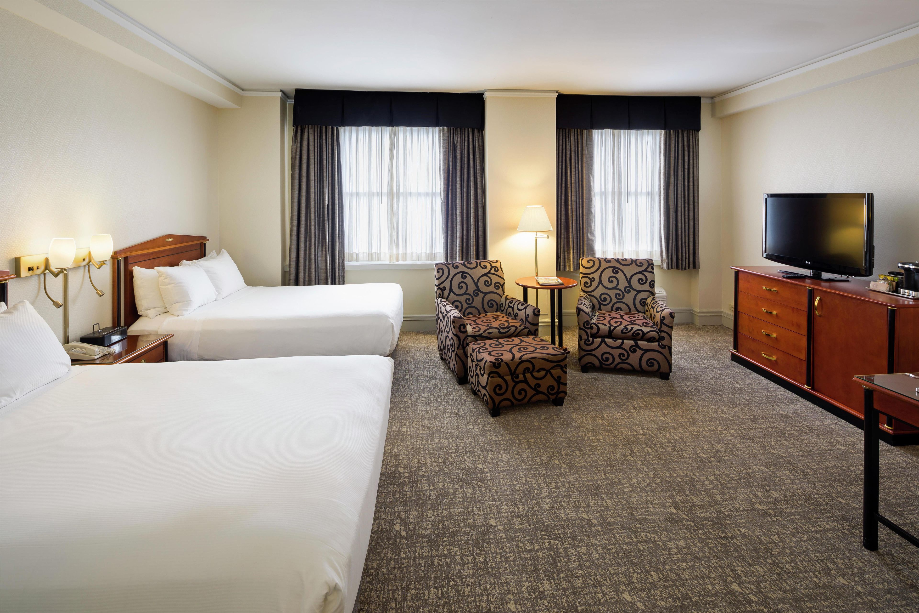 A hotel room with two beds, a television, a desk, and a chair.