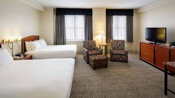 A hotel room with two beds, a television, a desk, and a chair.