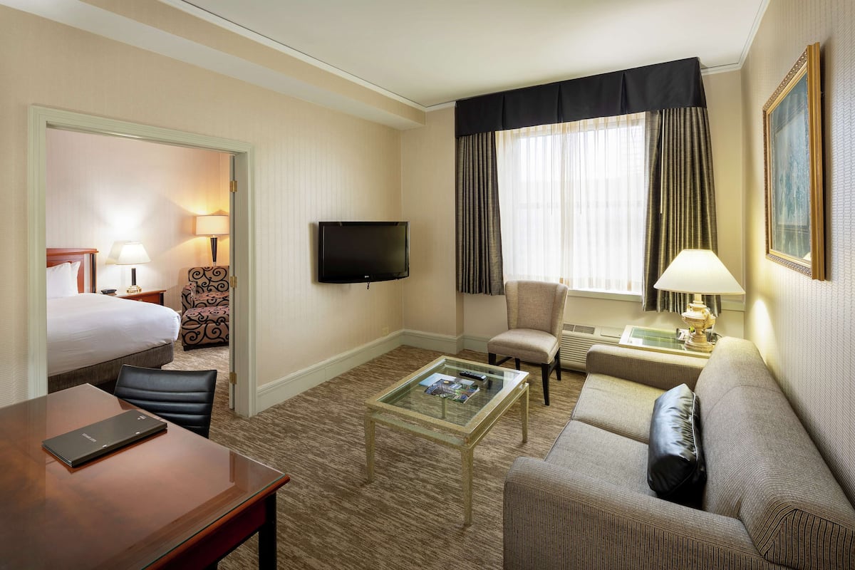 A hotel room with a bed, a desk, a sofa, a television, and a window with curtains.