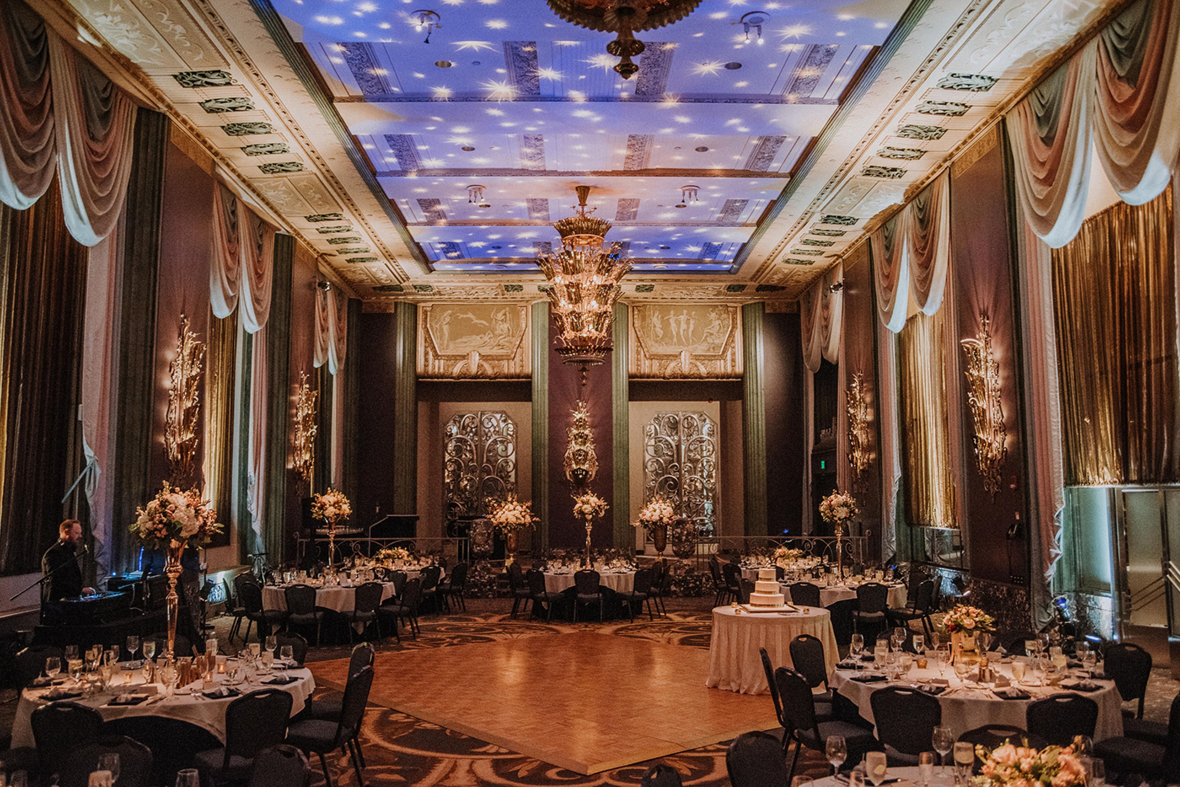 Un gran salón de baile con candelabros ornamentales, techos altos y un diseño de cielo estrellado.