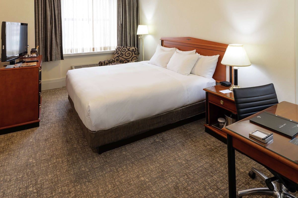 A hotel room with a large bed, a desk with a chair, a television, and a window with curtains.