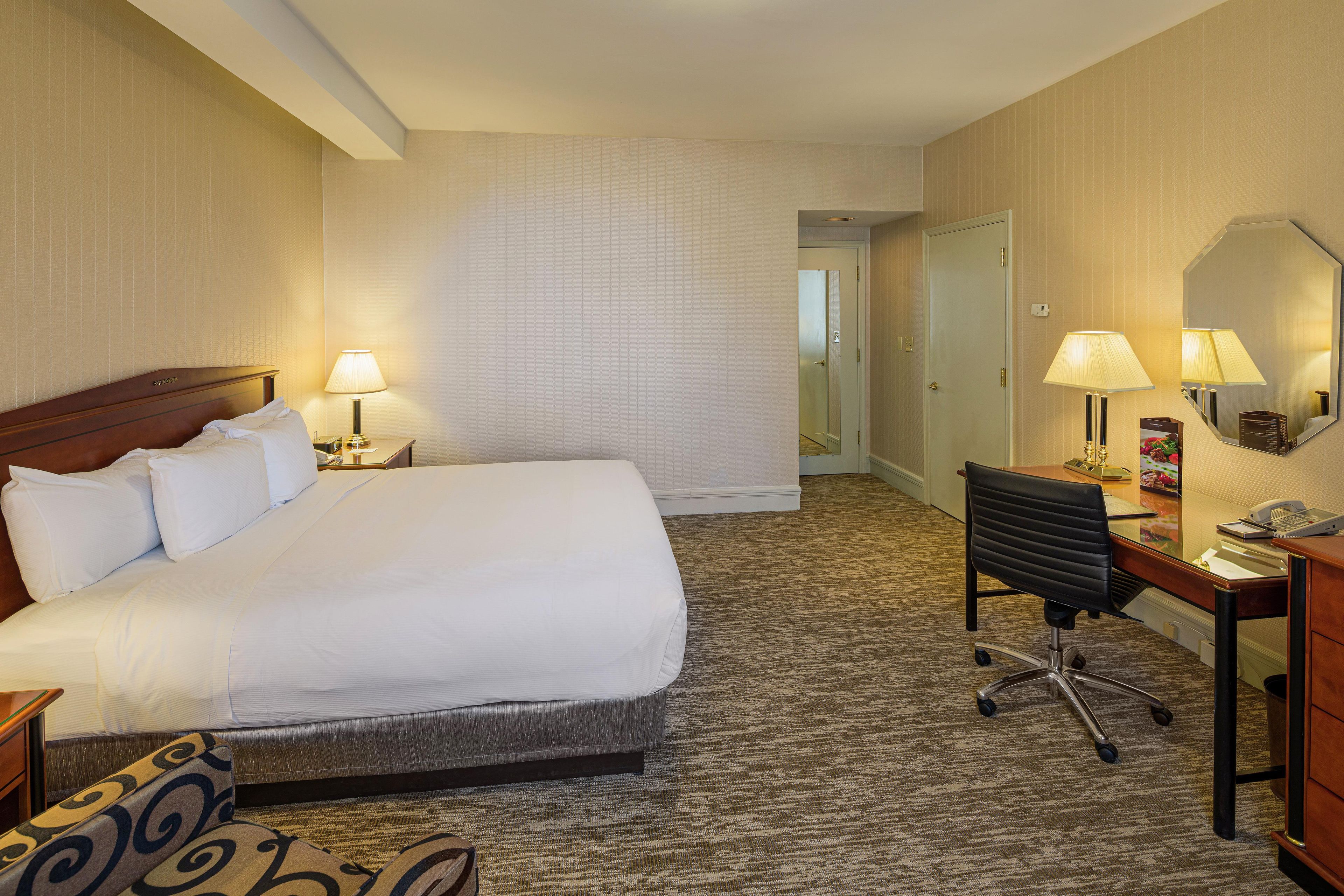 A hotel room with a large bed, a desk with a chair, a desk lamp, and a mirror.