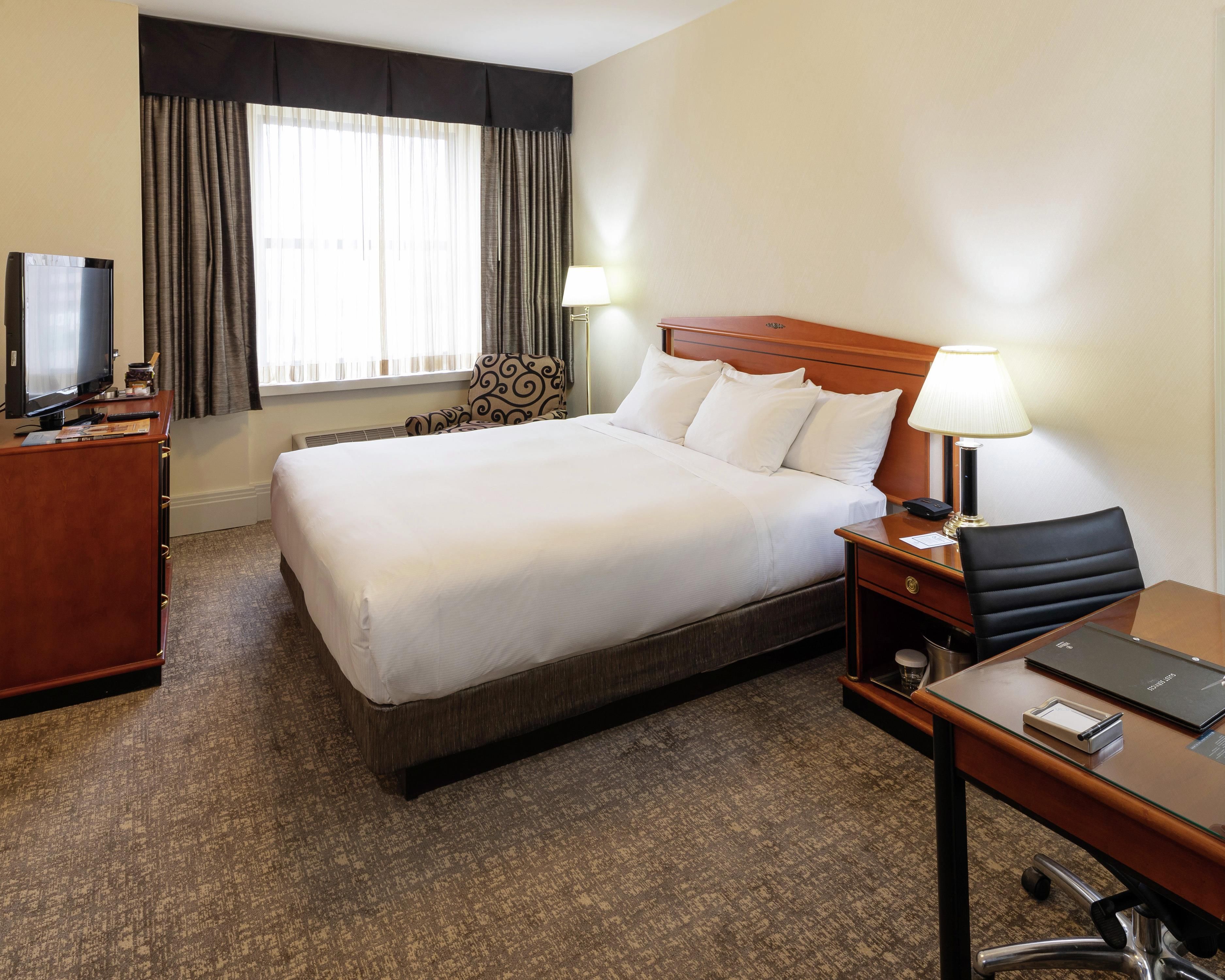 A hotel room with a bed, a desk, a chair, a television, and a window with curtains.