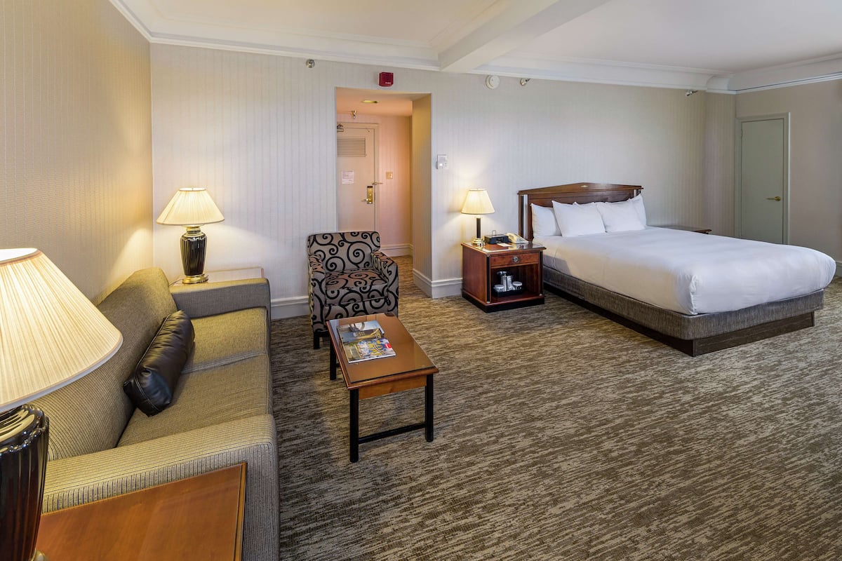 A hotel room with a bed, a sofa, a chair, a nightstand, and a table.