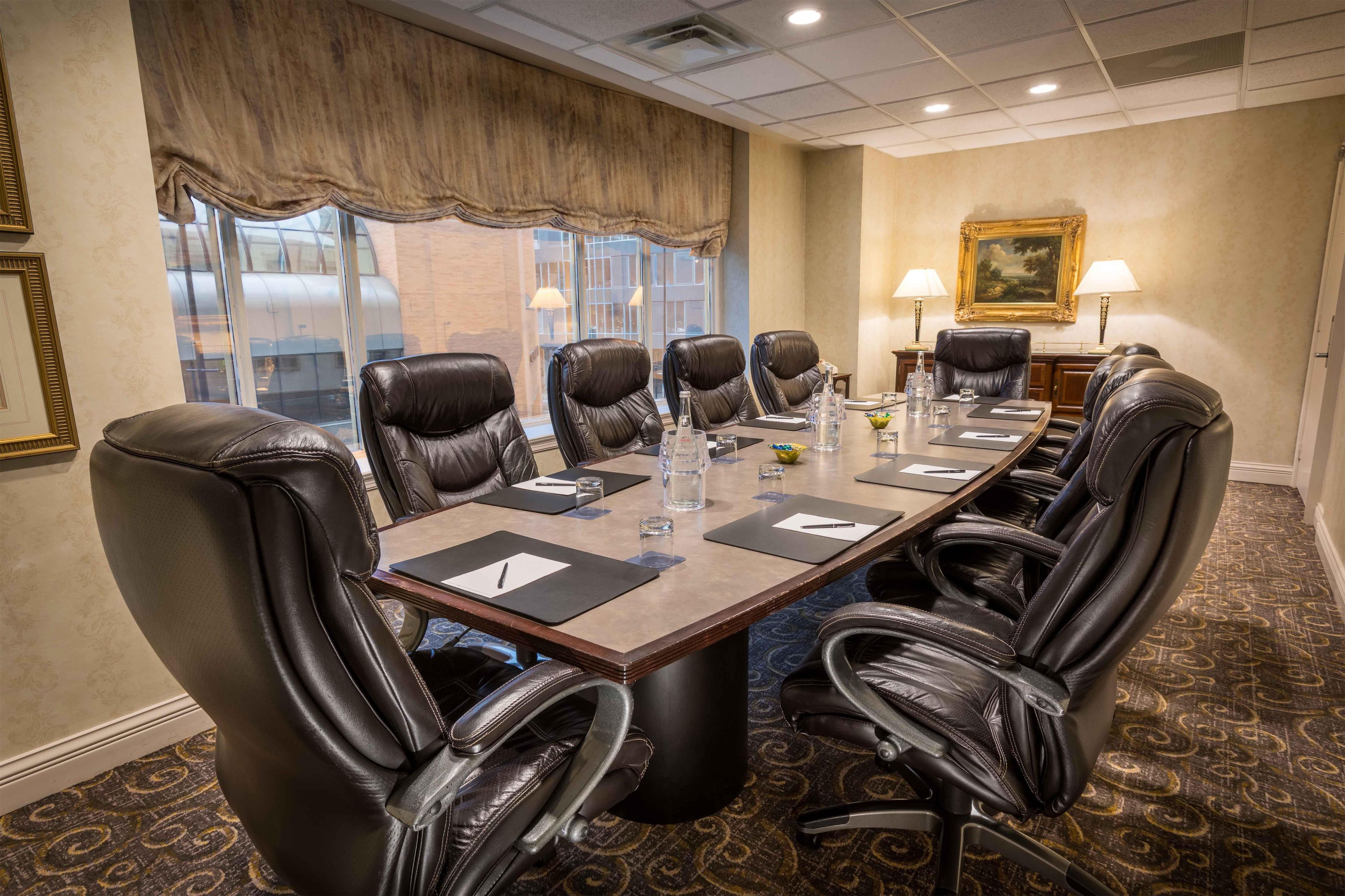 A conference room with a long table, black leather chairs, and a painting on the wall.