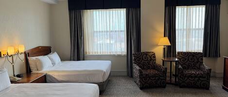 A hotel room with two beds, a chair, a table, and a lamp.