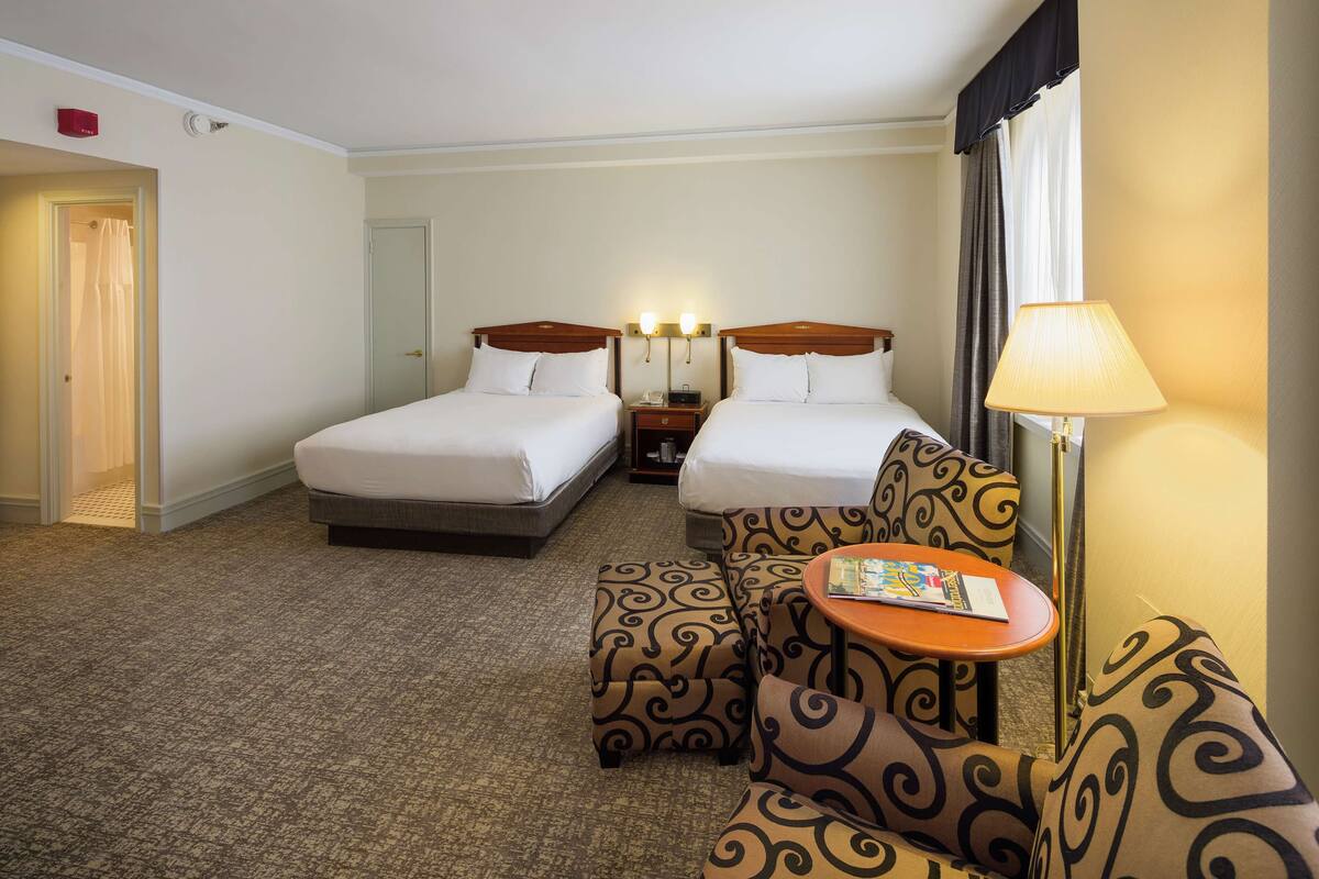 A hotel room with two beds, a sofa, a small table, and a lamp.